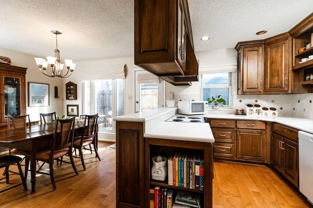 kitchen featuring white appliances, a chandelier, light wood-type flooring, kitchen peninsula, and decorative light fixtures