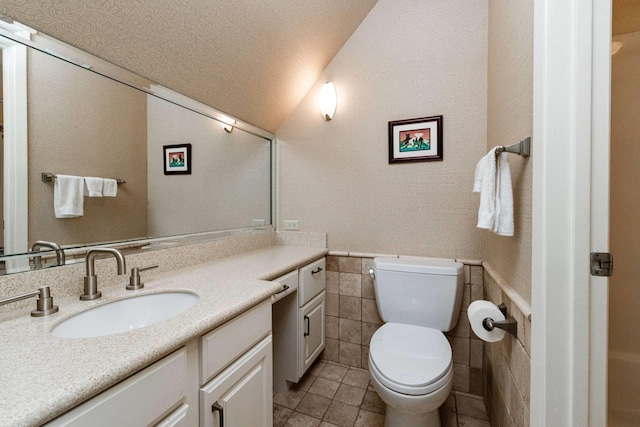 bathroom featuring toilet, tile patterned floors, vanity, tile walls, and a textured ceiling