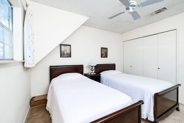 carpeted bedroom with ceiling fan, a closet, and a textured ceiling