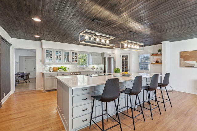 kitchen featuring a large island, a kitchen breakfast bar, stainless steel refrigerator, light hardwood / wood-style floors, and pendant lighting