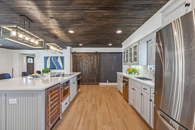 kitchen with a barn door, appliances with stainless steel finishes, hanging light fixtures, a kitchen island, and tasteful backsplash