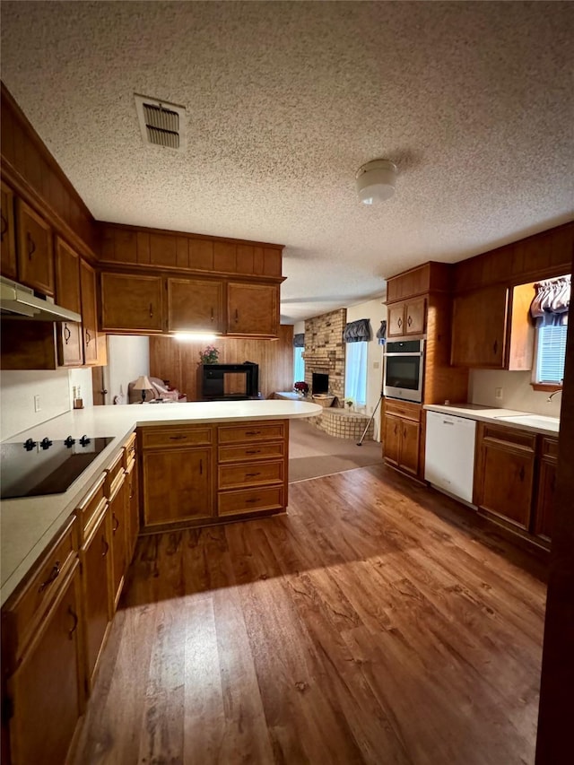 kitchen featuring kitchen peninsula, dishwasher, black electric cooktop, oven, and dark hardwood / wood-style flooring