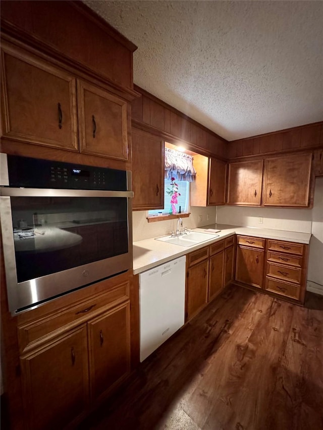 kitchen featuring stainless steel oven, white dishwasher, a textured ceiling, dark hardwood / wood-style floors, and sink