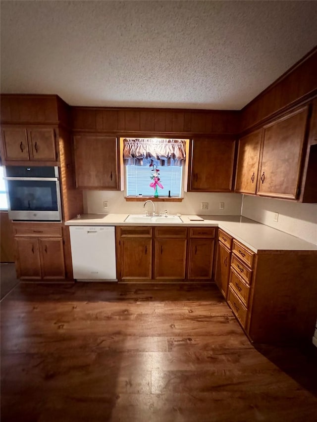 kitchen with sink, stainless steel oven, a textured ceiling, hardwood / wood-style flooring, and white dishwasher