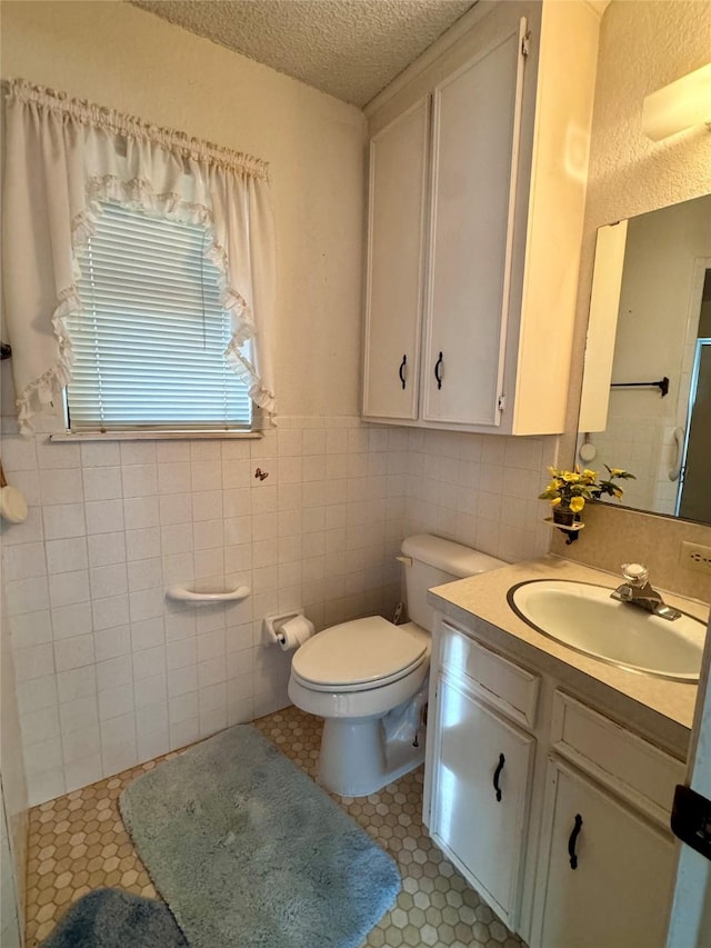 bathroom with toilet, a textured ceiling, tile walls, tile patterned floors, and vanity