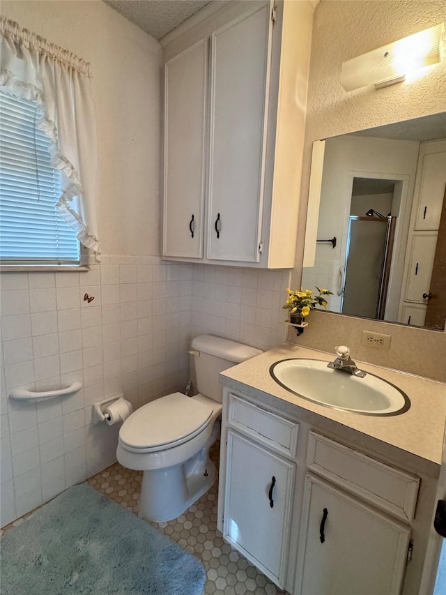 bathroom with toilet, vanity, tile patterned floors, tile walls, and a shower with shower door