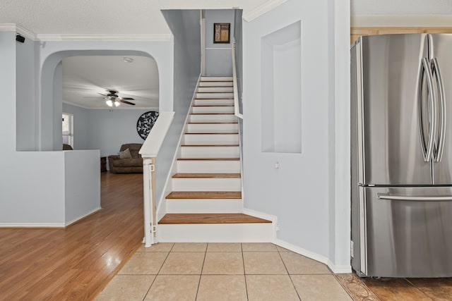 stairway with tile patterned flooring, crown molding, a ceiling fan, and arched walkways