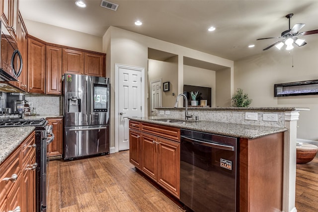 kitchen featuring hardwood / wood-style flooring, a center island with sink, appliances with stainless steel finishes, light stone counters, and sink