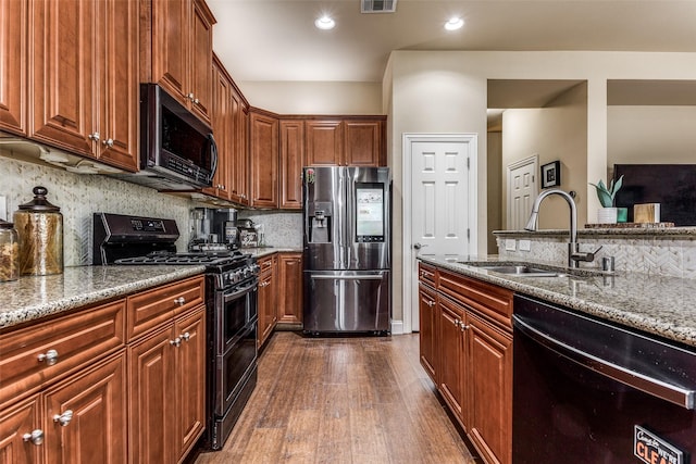 kitchen featuring backsplash, dark hardwood / wood-style flooring, light stone countertops, black appliances, and sink