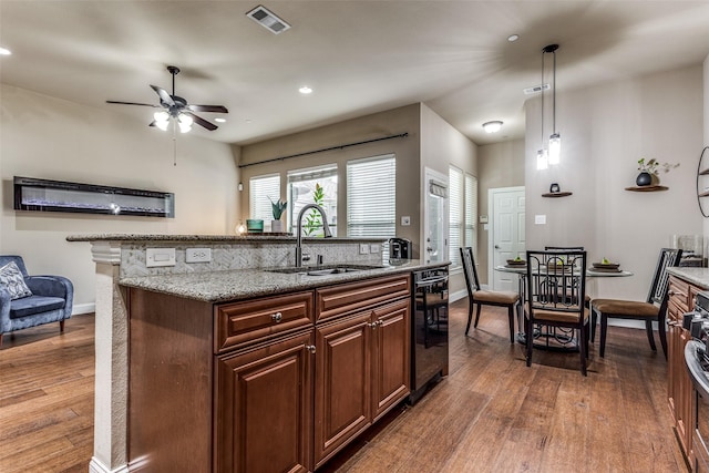 kitchen featuring sink, hanging light fixtures, a kitchen island with sink, light stone countertops, and dark hardwood / wood-style flooring