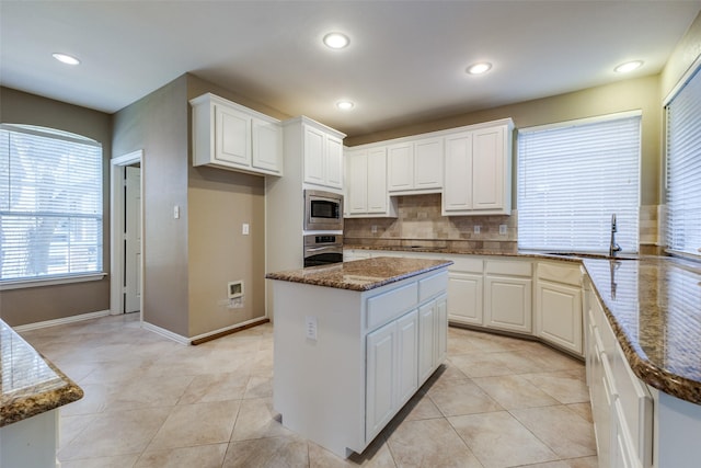 kitchen with stainless steel appliances, a kitchen island, white cabinetry, and dark stone countertops