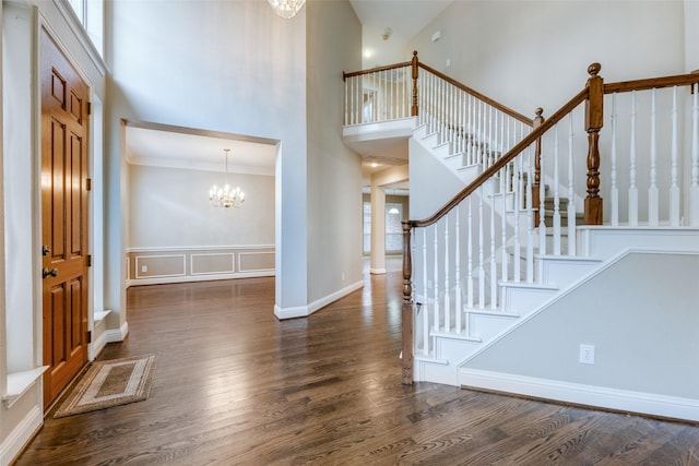 entryway featuring a towering ceiling, a chandelier, crown molding, and dark wood-type flooring