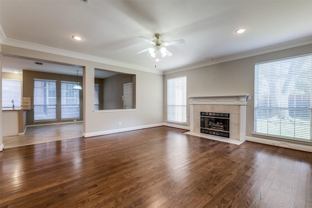 unfurnished living room featuring dark wood-type flooring, a tiled fireplace, ceiling fan, and crown molding