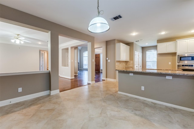 kitchen featuring light stone countertops, stainless steel appliances, decorative backsplash, white cabinets, and ceiling fan