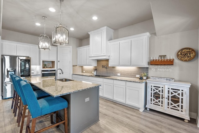 kitchen featuring light stone counters, a center island with sink, white cabinets, appliances with stainless steel finishes, and sink