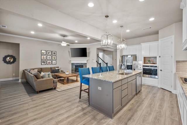 kitchen featuring a kitchen island with sink, a breakfast bar area, stainless steel appliances, a fireplace, and white cabinets