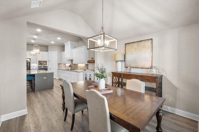 dining room with sink, light hardwood / wood-style flooring, and vaulted ceiling