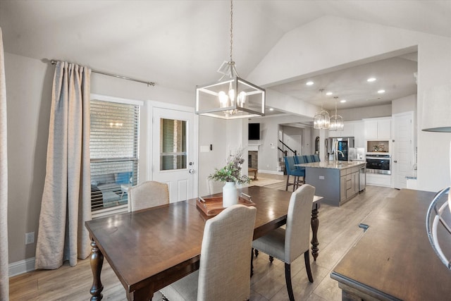 dining room with sink, an inviting chandelier, vaulted ceiling, light hardwood / wood-style flooring, and a brick fireplace