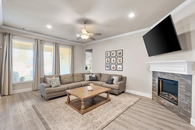 living room featuring light hardwood / wood-style floors, ceiling fan, a tiled fireplace, and crown molding