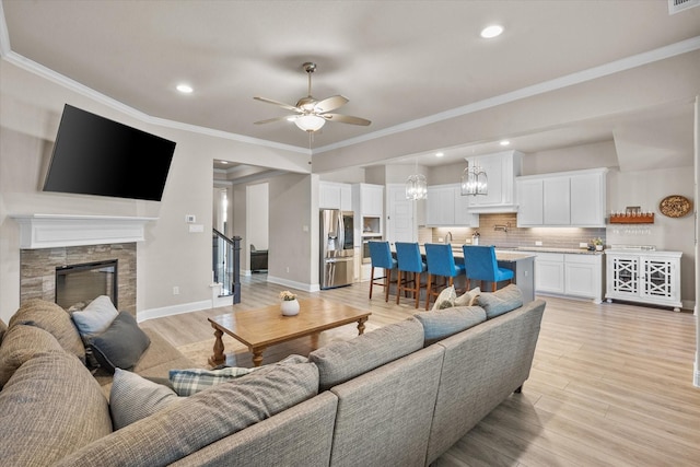 living room with ornamental molding, ceiling fan with notable chandelier, light hardwood / wood-style flooring, and a fireplace