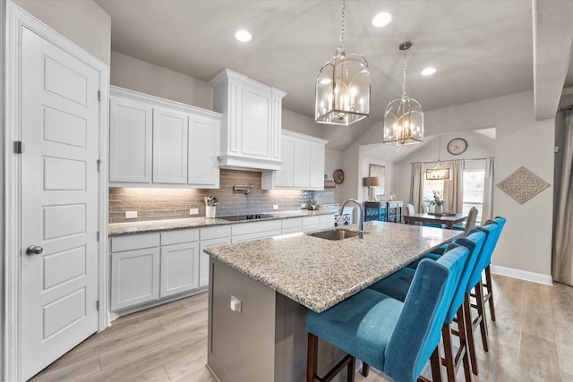 kitchen featuring light stone counters, hanging light fixtures, a center island with sink, black electric cooktop, and white cabinetry