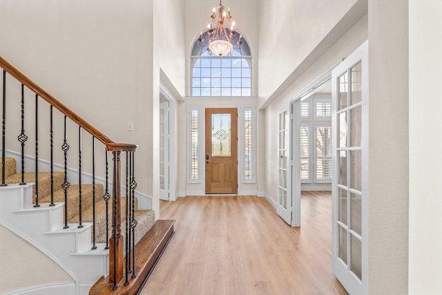 entryway featuring a towering ceiling, light wood-type flooring, french doors, and an inviting chandelier