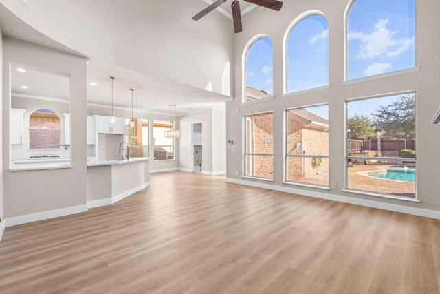 unfurnished living room featuring sink, ceiling fan, light hardwood / wood-style flooring, a high ceiling, and crown molding