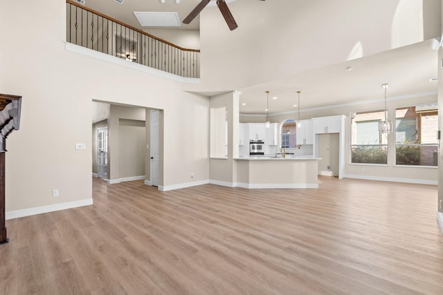 unfurnished living room featuring sink, a towering ceiling, ceiling fan, light hardwood / wood-style flooring, and crown molding