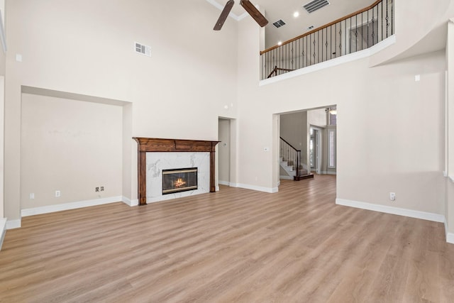 unfurnished living room featuring light hardwood / wood-style floors, a premium fireplace, a towering ceiling, and ceiling fan