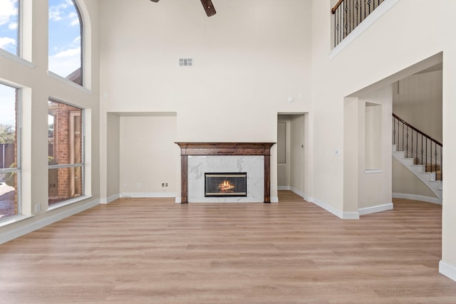 unfurnished living room with a high ceiling, a high end fireplace, and ceiling fan