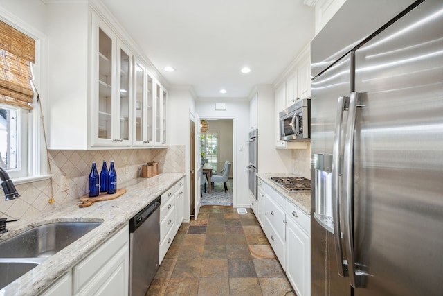 kitchen featuring appliances with stainless steel finishes, light stone countertops, sink, white cabinets, and tasteful backsplash