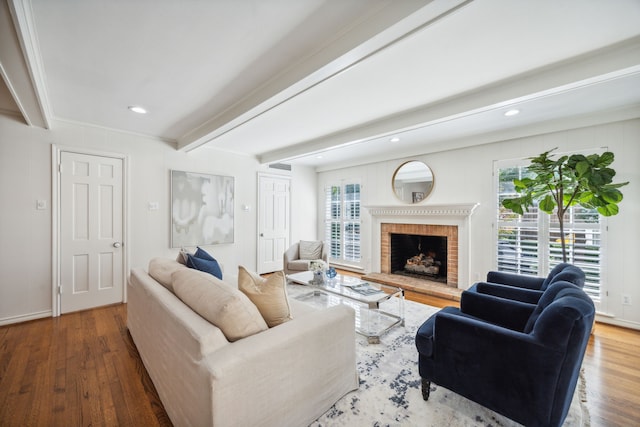 living room with wood-type flooring, a brick fireplace, plenty of natural light, and beamed ceiling