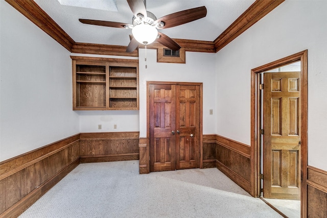 spare room featuring ceiling fan, light colored carpet, a wainscoted wall, wood walls, and crown molding