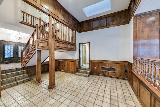 interior space with a skylight, visible vents, a towering ceiling, a wainscoted wall, and stairs