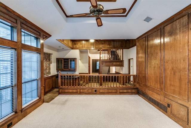 living room featuring ceiling fan, wooden walls, a tray ceiling, a wealth of natural light, and light colored carpet