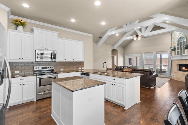 kitchen with dark stone countertops, stainless steel appliances, beamed ceiling, a kitchen island, and sink