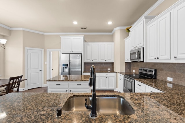 kitchen with dark stone countertops, stainless steel appliances, decorative backsplash, sink, and white cabinetry