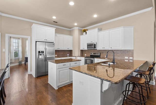 kitchen with kitchen peninsula, white cabinetry, appliances with stainless steel finishes, dark stone countertops, and sink