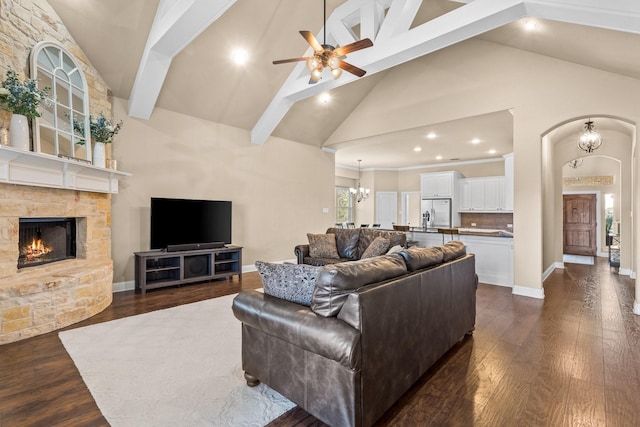 living room featuring ceiling fan with notable chandelier, high vaulted ceiling, dark hardwood / wood-style floors, and a stone fireplace