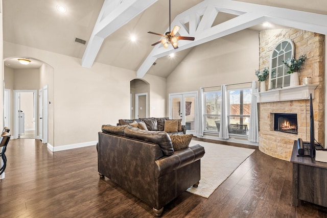 living room with a stone fireplace, ceiling fan, high vaulted ceiling, beam ceiling, and dark wood-type flooring