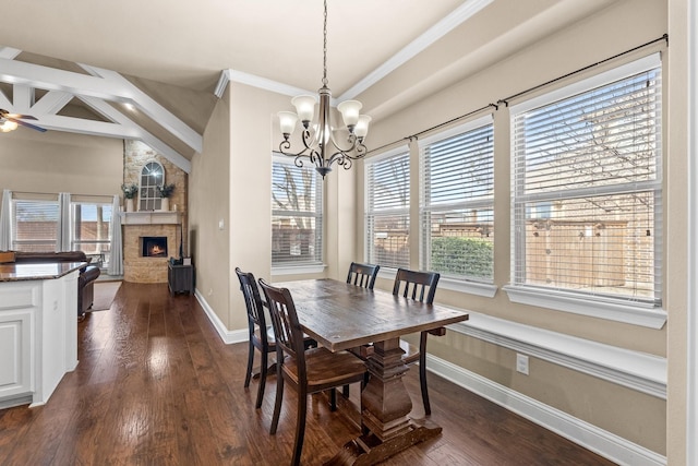 dining space with dark wood-type flooring, beam ceiling, crown molding, ceiling fan with notable chandelier, and a stone fireplace