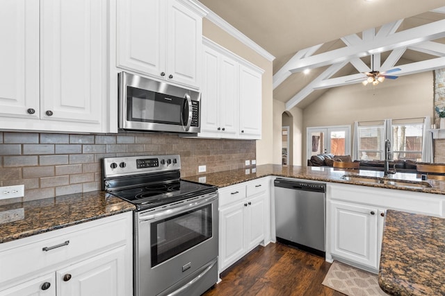 kitchen with stainless steel appliances, sink, white cabinetry, dark stone countertops, and beam ceiling