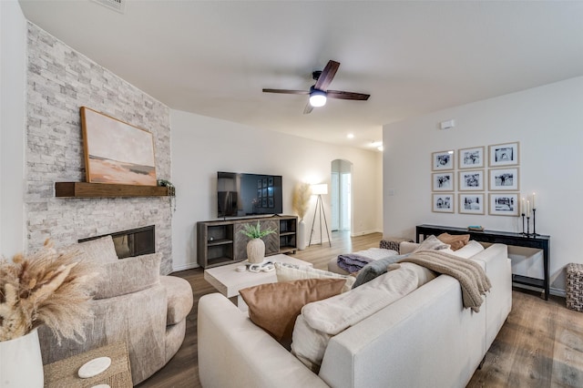 living room featuring ceiling fan, a stone fireplace, and wood-type flooring