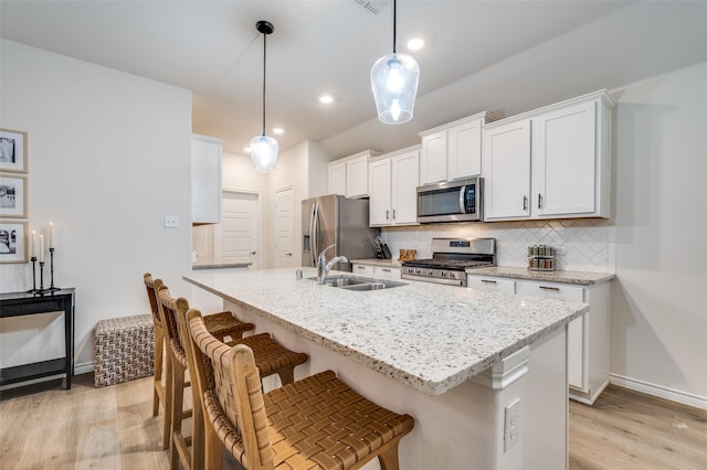 kitchen with stainless steel appliances, sink, decorative light fixtures, white cabinetry, and backsplash