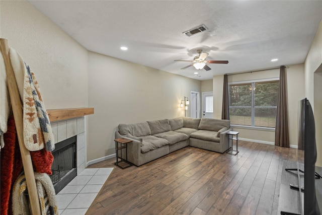 living room with a tile fireplace, a textured ceiling, ceiling fan, and light hardwood / wood-style floors