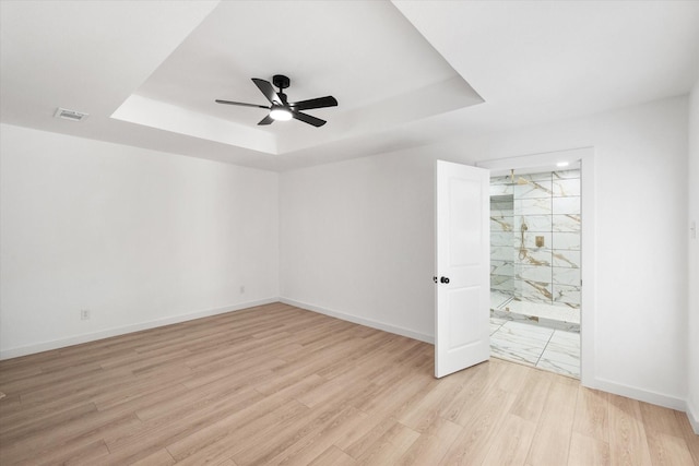 spare room with a raised ceiling, ceiling fan, and light hardwood / wood-style flooring