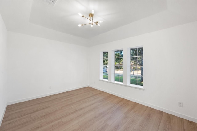 empty room featuring a raised ceiling, light wood-type flooring, and a chandelier