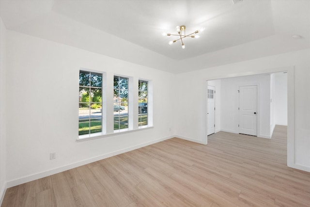 unfurnished room featuring a tray ceiling, light hardwood / wood-style flooring, and a chandelier