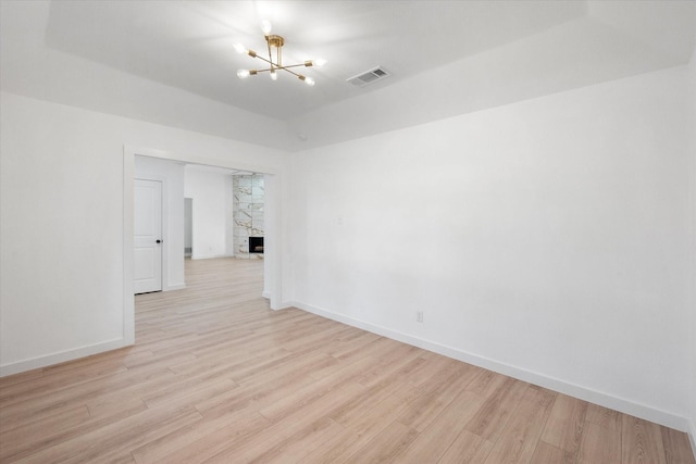 spare room with a notable chandelier, light hardwood / wood-style floors, and a fireplace