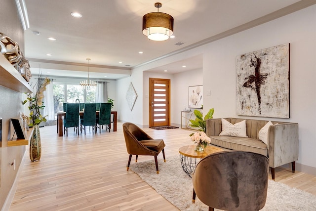 living room featuring light wood-type flooring, a notable chandelier, and crown molding